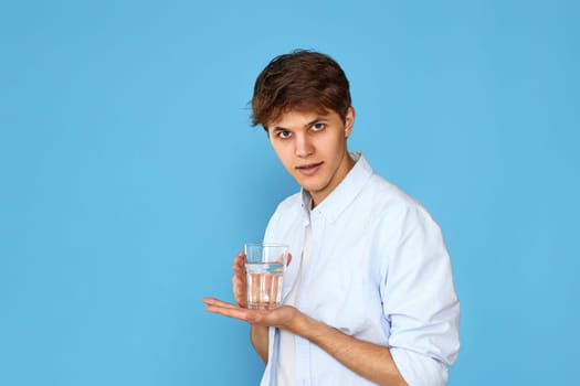 Young handsome man with glass of water on blue background