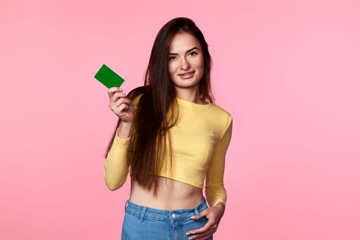 pretty woman in yellow clothes holding plastic credit card isolated on pink background