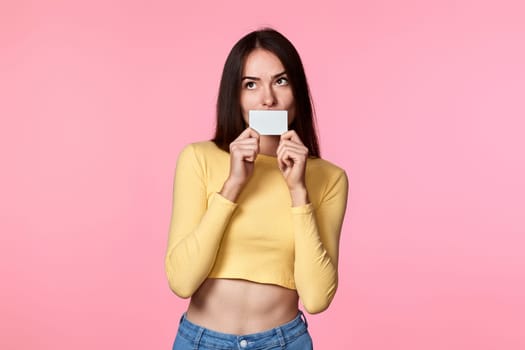 young woman in yellow clothes holding plastic credit card isolated on pink background