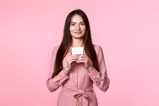young woman in pink dress holding plastic credit card isolated on pink background
