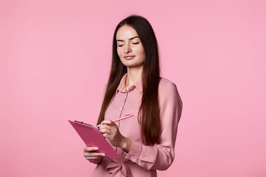 beautiful brunette business woman holding clipboard with papers document on pink background.