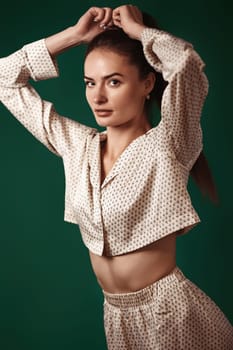 sexy brunette woman wear natural organic silk suit pants and blouse on dark green background.