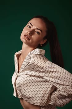 sexy brunette woman wear natural organic silk suit pants and blouse on dark green background.