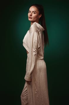 sexy brunette woman wear natural organic silk suit pants and blouse on dark green background.