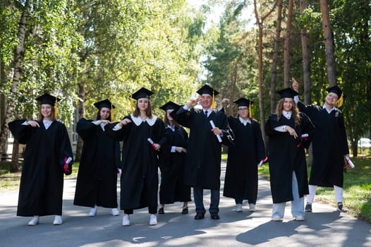 Group of graduates in robes dancing outdoors. Elderly student