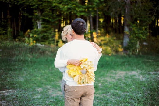 Man hugs woman with a wreath of yellow leaves in her hands. Back view. High quality photo