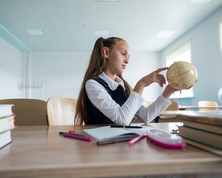 Caucasian schoolgirl sits at her desk at school and studies the globe