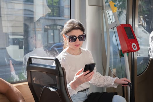 Young brunette browsing and typing messages on phone on way to work in tram, High quality photo