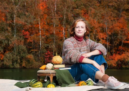 beautiful red-haired girl observes enjoys beautiful autumn nature sitting on a raft near a forest lake. High quality photo