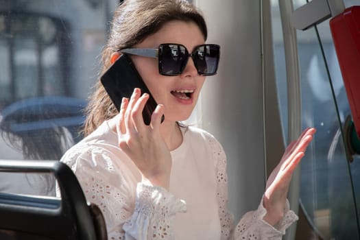 Millennial brunette in sunglasses talking on the phone in a tram by the window, High quality photo