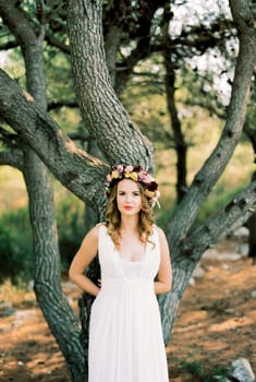 Bride in a wreath on her head leans on a tree. High quality photo