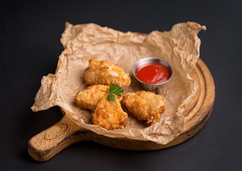 chicken fillet fried in batter with sauce on a wooden board on a black background