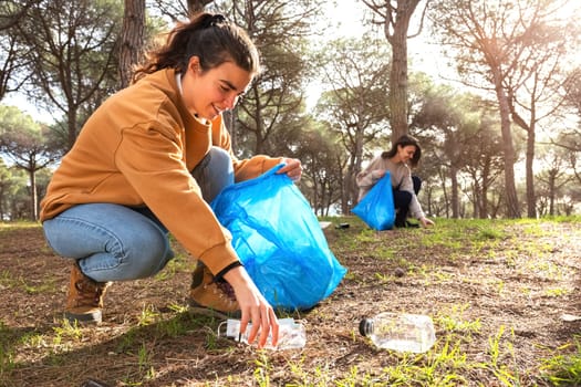 Happy young caucasian women activists pick up plastic trash to clean forest. Ecology concept. Environmental preservation.