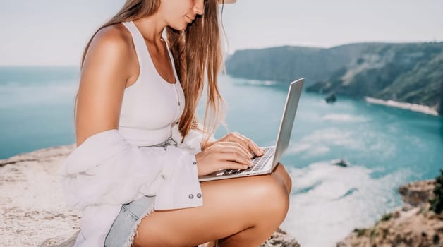 Digital nomad, Business woman working on laptop by the sea. Pretty lady typing on computer by the sea at sunset, makes a business transaction online from a distance. Freelance remote work on vacation