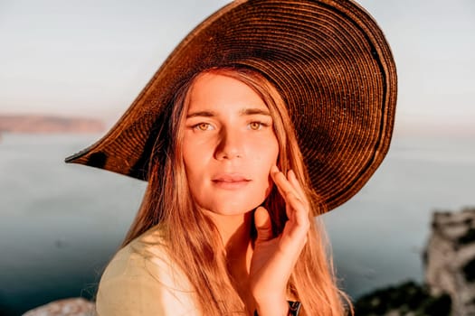 Portrait of happy young woman wearing summer black hat with large brim at beach on sunset. Closeup face of attractive girl with black straw hat. Happy young woman smiling and looking at camera at sea