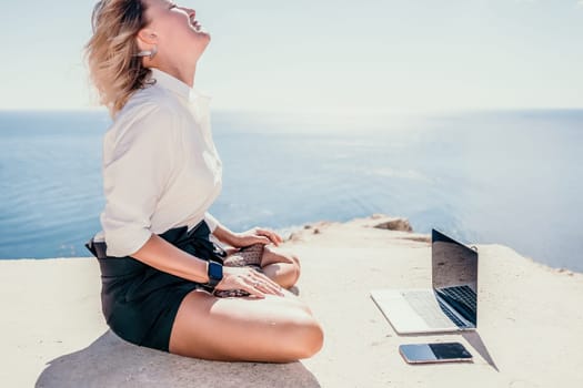 Happy girl doing yoga with laptop working at the beach. beautiful and calm business woman sitting with a laptop in a summer cafe in the lotus position meditating and relaxing. freelance girl remote work beach paradise