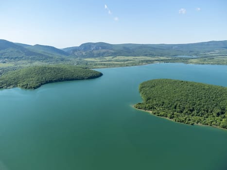 Aerial landscape from flying drone storage reservoir at mountain foot covered colorful spring forest. Beautiful view from above blue lake among highlands