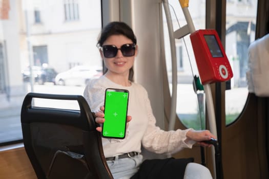 brunette woman showing smartphone with vertical green screen in tram, next to the digital checkout High quality photo