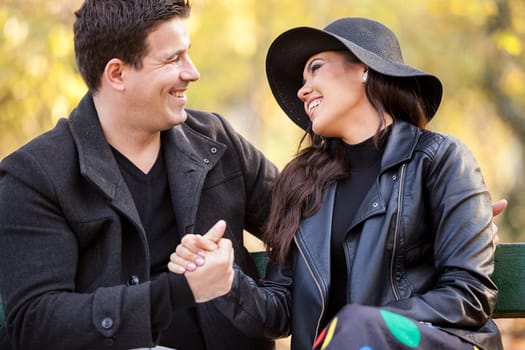 Close up of smiling in love couple sitting on a bench in autumn park