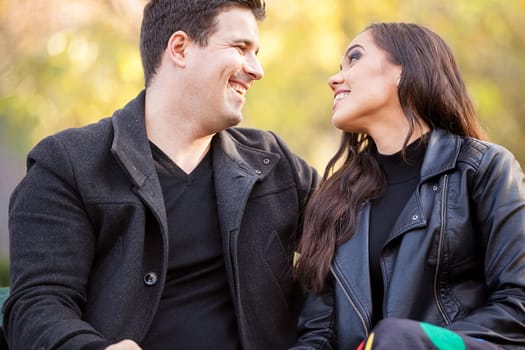 Close up of smiling in love couple sitting on a bench in autumn park