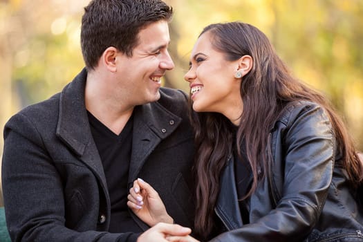 Close up of happy beautiful in love couple sitting on a bench in autumn park