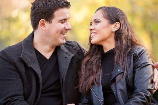 Close up of happy beautiful in love couple sitting on a bench in autumn park