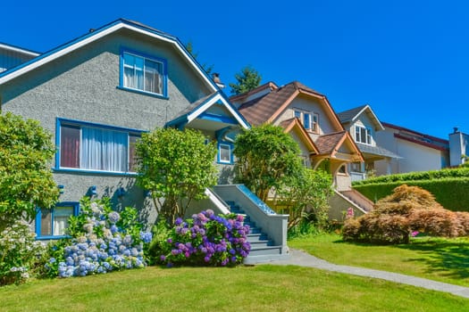 Snug warm family houses side by side. Residential house with the pathway over front yard lawn on blue sky background.