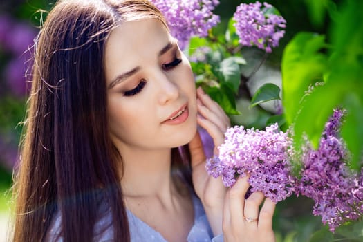 Close up of beautiful brunette girl stands with lilac flowers, in the park