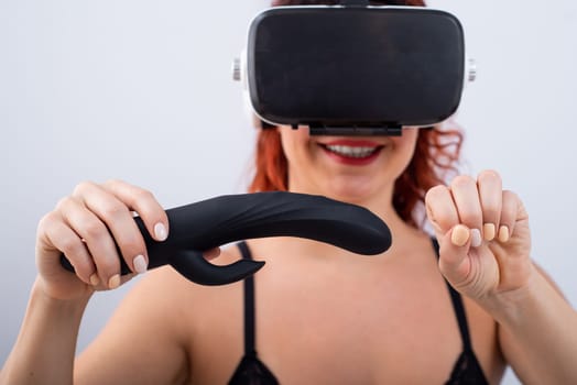 Woman in VR glasses with a black dildo on a white background. The girl masturbates and watches 3d porn.