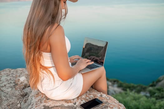 Freelance women sea working on the computer. Good looking middle aged woman typing on a laptop keyboard outdoors with a beautiful sea view. The concept of remote work