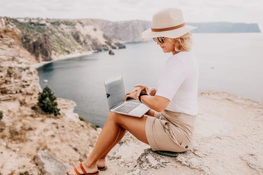 Digital nomad, Business woman working on laptop by the sea. Pretty lady typing on computer by the sea at sunset, makes a business transaction online from a distance. Freelance remote work on vacation