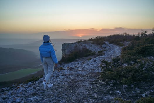 Woman tourist on top of sunrise mountain. The girl salutes the sun, wearing a blue jacket, white hat and white jeans. Conceptual design