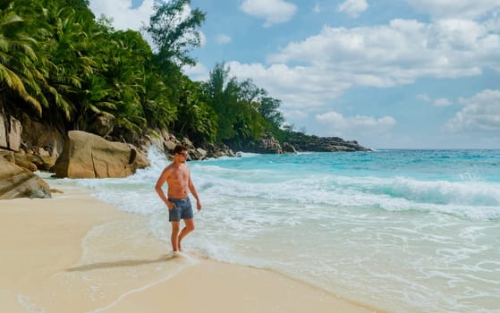 Young men in a swim short on a white tropical beach with palm trees Petite Anse beach Mahe Tropical Seychelles Islands.