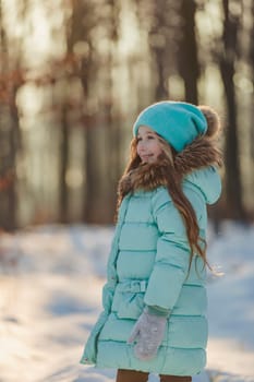 girl in a turquoise squat and a hat in a winter forest, shot vertically