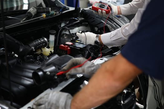 Professional auto mechanic works in a car service and tests operation of engine with tester. Mechanical service using multimeter to check voltage level in car battery