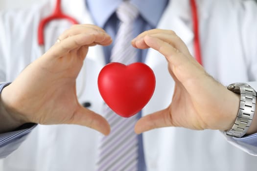 Hands of doctor cardiologist hold red toy heart in air. Cardiology care and health insurance concept