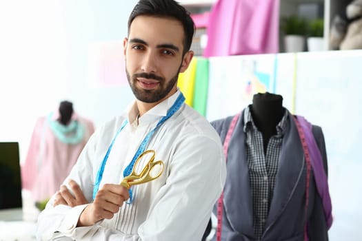 Smiling handsome fashion designer with scissors standing next to mannequin at workplace. Male fashion designer stylist concept