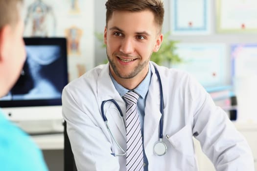 Young smiling male doctor in medical uniform takes patient. Smiling and chatting in medical clinic