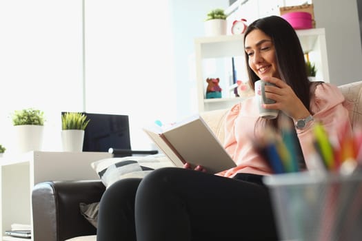 Happy cheerful female reader enjoying novel on sofa. Smiling woman enjoying book novel hobby and home leisure