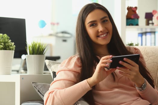 Relaxed smiling woman on sofa at home using smartphone and texting. Chat communication and mobile apps concept