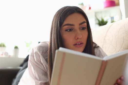 Portrait of pensive smart woman reading book at home and relaxing on sofa. Home leisure concept