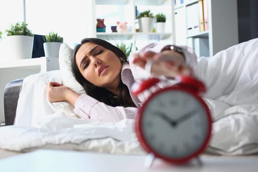 Dissatisfied woman lies in bed and turns off alarm clock. Irritated young woman turns off the alarm clock in the morning