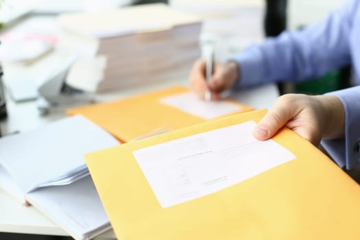 Secretary fills in address on yellow postal envelope for sending letters. Business correspondence and documentation concept