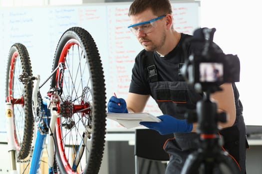 Young handsome male blogger is inspecting broken bike on camera. Remote repair of bicycle equipment concept