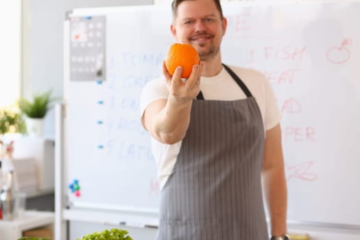 Male blogger cook holding orange and giving training lesson on how to cook healthy food. Remote training of chef profession