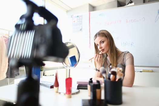 Beautiful blogger girl does tutorial makeup on camera in blog. Makeup brushes and palettes on table and online learning concept