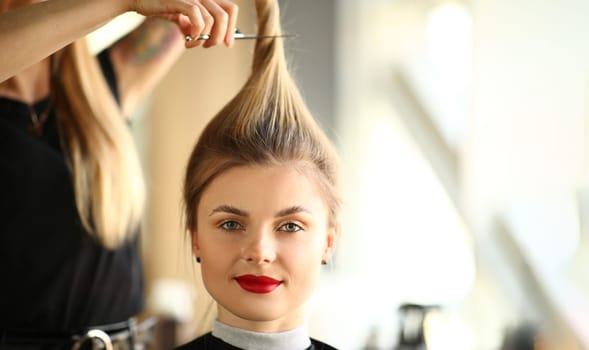 Portrait of blonde woman in hairdressing salon with long ponytail. Master hairdresser cuts hair concept