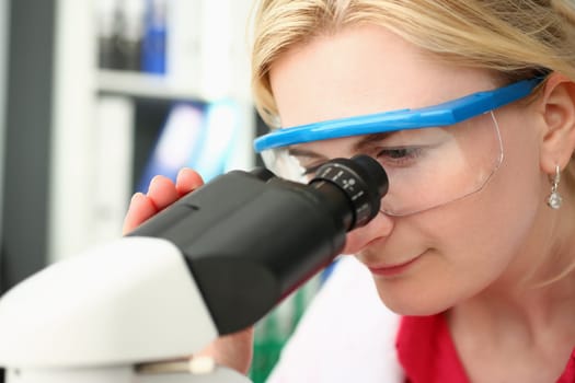 Portrait of focused female scientist looking through microscope in laboratory. Young scientist doing medical research