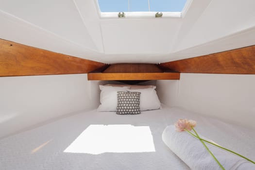Bright luxury comfortable yacht inside with wood trim with white terry sheets, pillows, flower and sunbeams breaking through. Concept of luxury vacation on your own small yacht