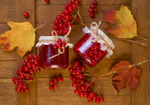 Viburnum fruit jam in a glass jar on a wooden table, preparations for the winter